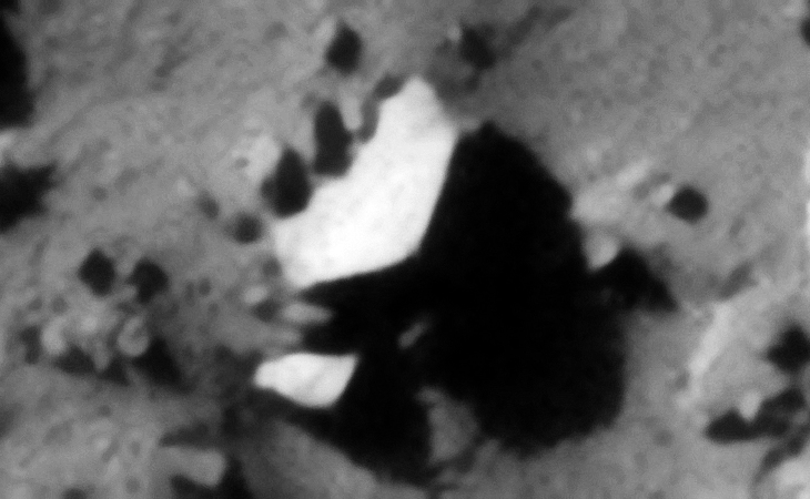 A partially buried, bright metallic-type hexagonal object with straight edges and rounded corner. Another bright piece is sticking out to the bottom left of the image