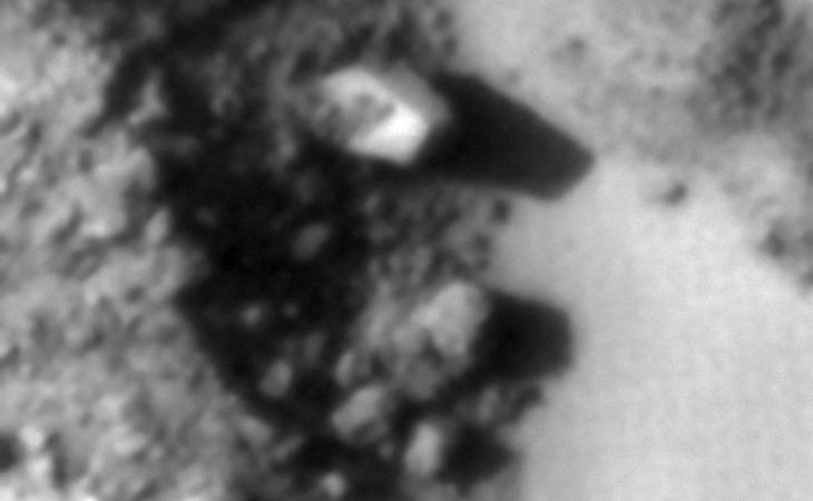 A bright, triangular object sticking out of the side of a small mound, parts of a machine seems to be strewn about